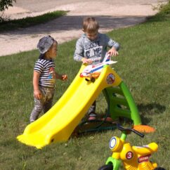 Kollane liumägi muru peal koos kahe poisiga, kes kasutavad liumäge lennuki hoovõturajana.