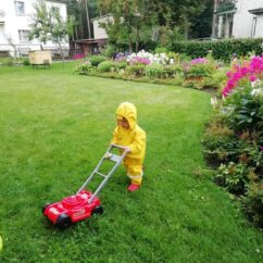 Kollase kostüümiga laps muruplatsil punase muruniidukiga.