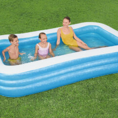 Suur täispuhutav bassein murul milles on täiskasvanu ja lapsed.