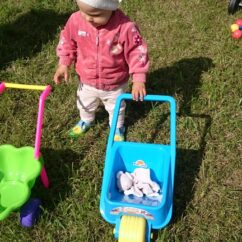 Väike laps muruplatsil koos kahe aiakäruga, millest ta mõlema käega kinni hoiab.